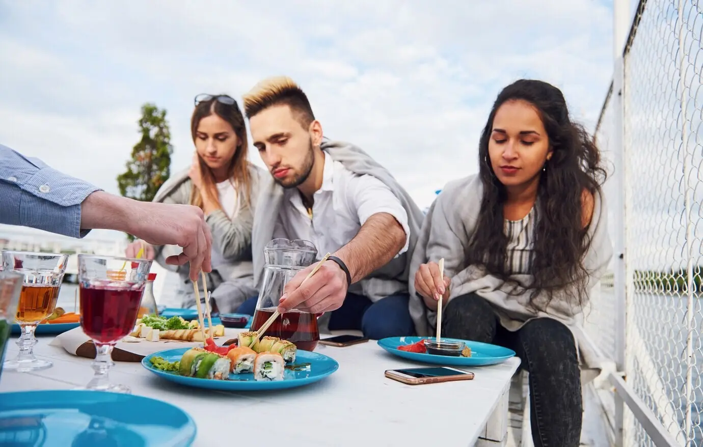 Joyful young friends were sitting at a table, having a picnic outdoors.